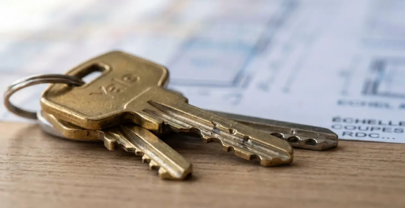 Gros plan rapproché de clés métalliques posées sur un document architectural flouté avec faible profondeur de champ